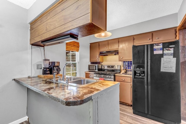 kitchen with appliances with stainless steel finishes, backsplash, kitchen peninsula, light wood-type flooring, and sink