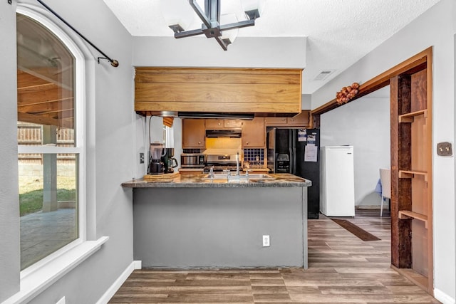 kitchen with kitchen peninsula, a textured ceiling, stainless steel range oven, dark hardwood / wood-style floors, and black fridge