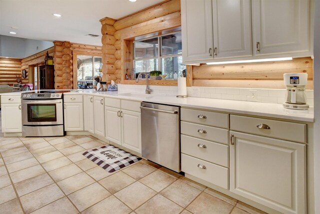 kitchen featuring white cabinets, light tile patterned floors, stainless steel appliances, sink, and rustic walls