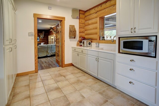 kitchen featuring stainless steel microwave, rustic walls, and white cabinets