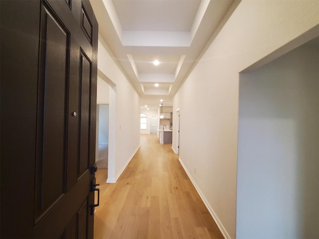 hallway featuring sink, a tray ceiling, and light wood-type flooring