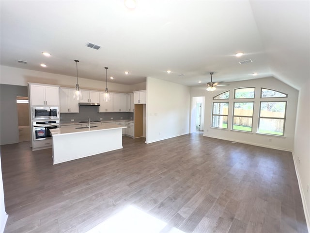 kitchen featuring built in microwave, oven, pendant lighting, a kitchen island with sink, and white cabinets