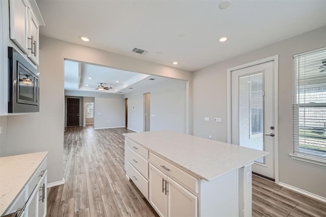 kitchen with light hardwood / wood-style floors, white cabinetry, stainless steel microwave, and a kitchen island