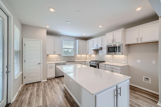 kitchen with white cabinetry, sink, stainless steel appliances, a kitchen island, and light wood-type flooring