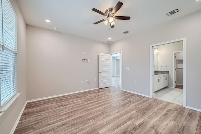 unfurnished bedroom featuring light wood-type flooring, ensuite bathroom, and multiple windows