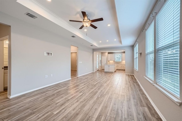 unfurnished living room with ceiling fan, a raised ceiling, light wood-type flooring, and crown molding