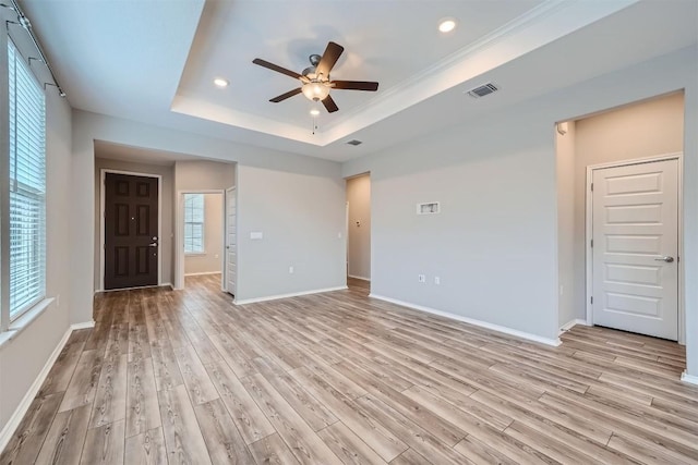 empty room with ceiling fan, light hardwood / wood-style floors, a raised ceiling, and crown molding