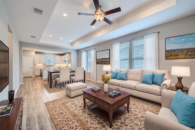 living room with plenty of natural light, light hardwood / wood-style floors, a raised ceiling, and ceiling fan