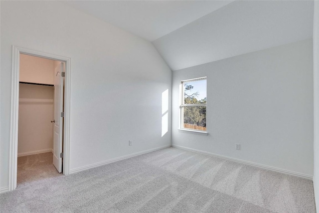 unfurnished bedroom featuring light carpet, a spacious closet, and vaulted ceiling