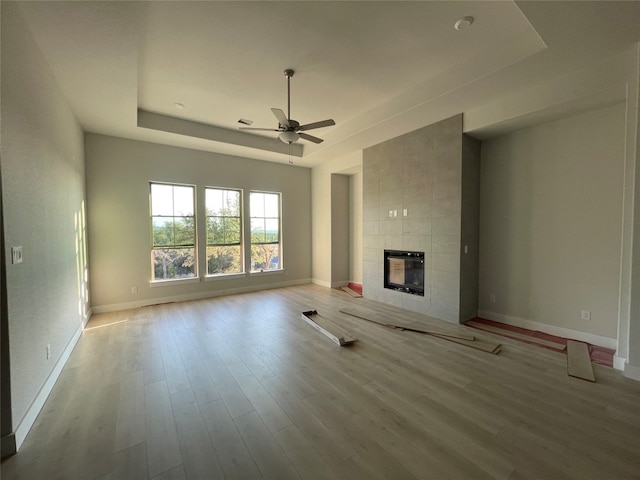 unfurnished living room with ceiling fan, a tile fireplace, light hardwood / wood-style floors, and a raised ceiling