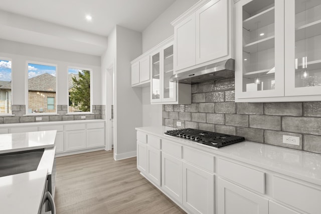 kitchen featuring light hardwood / wood-style flooring, white cabinetry, stainless steel gas cooktop, decorative backsplash, and wall chimney exhaust hood