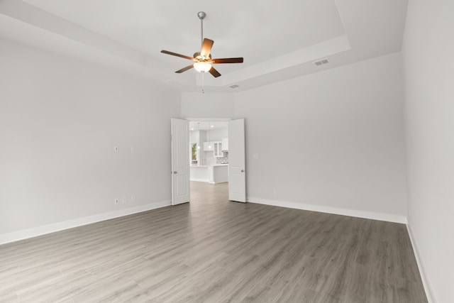 empty room featuring a raised ceiling, hardwood / wood-style flooring, and ceiling fan