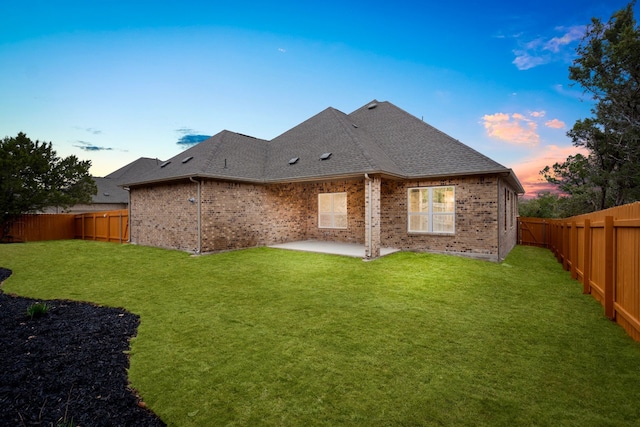 back house at dusk featuring a patio area and a lawn