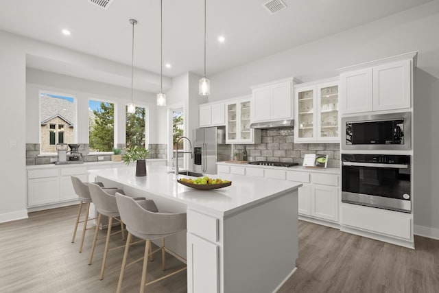 kitchen with hanging light fixtures, an island with sink, white cabinets, and appliances with stainless steel finishes