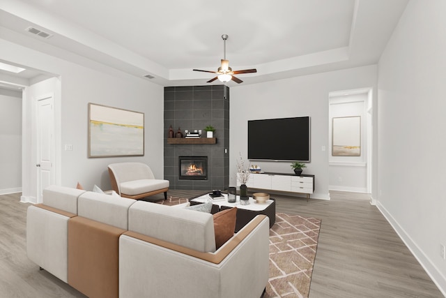 living room with wood-type flooring, a tile fireplace, a raised ceiling, and ceiling fan