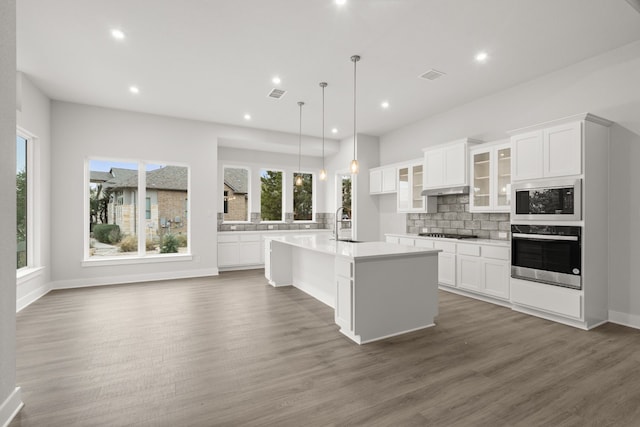 kitchen featuring white cabinetry, a center island with sink, oven, and decorative light fixtures