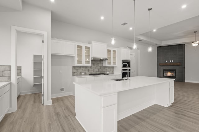 kitchen featuring hanging light fixtures, gas cooktop, a kitchen island with sink, decorative backsplash, and white cabinets