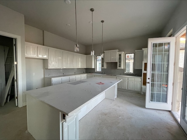 kitchen featuring tasteful backsplash, light stone counters, a kitchen island, decorative light fixtures, and white cabinetry