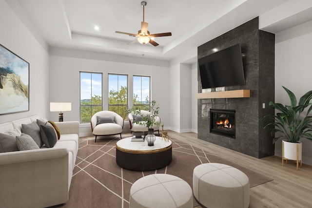 living room featuring a tile fireplace, wood-type flooring, ceiling fan, and a tray ceiling