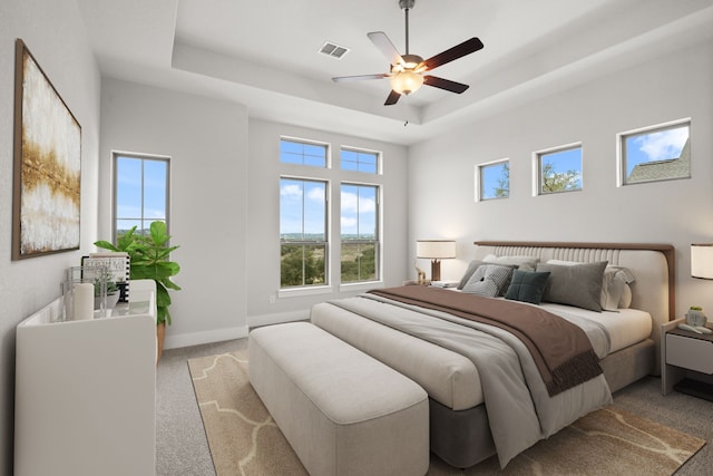 bedroom featuring ceiling fan, a raised ceiling, and light colored carpet