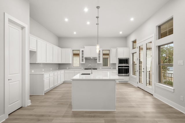 kitchen featuring hanging light fixtures, a center island with sink, stainless steel appliances, decorative backsplash, and white cabinets