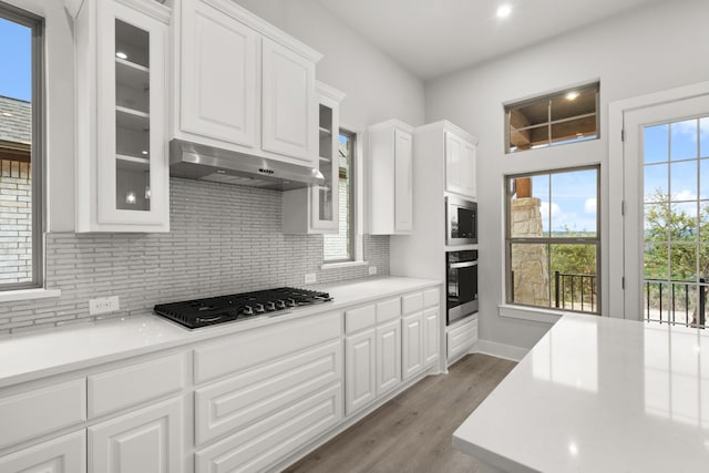 kitchen with range hood, white cabinets, backsplash, stainless steel appliances, and light hardwood / wood-style flooring