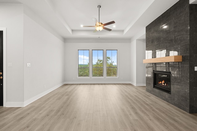 unfurnished living room with a tiled fireplace, light hardwood / wood-style floors, a raised ceiling, and ceiling fan