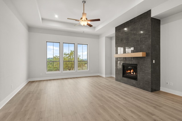 unfurnished living room featuring a tiled fireplace, a tray ceiling, light hardwood / wood-style floors, and ceiling fan