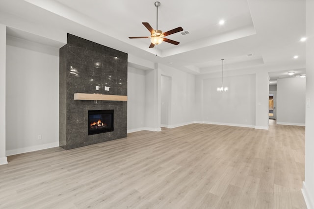 unfurnished living room with ceiling fan with notable chandelier, light hardwood / wood-style flooring, a fireplace, and a tray ceiling