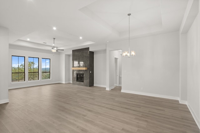 unfurnished living room with a fireplace, a tray ceiling, ceiling fan with notable chandelier, and hardwood / wood-style floors