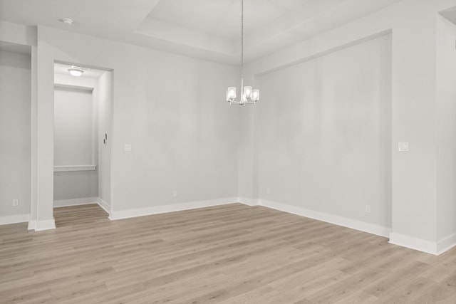 empty room featuring an inviting chandelier, light wood-type flooring, and a tray ceiling