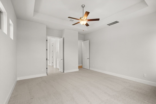 unfurnished bedroom featuring ceiling fan, a tray ceiling, and light colored carpet