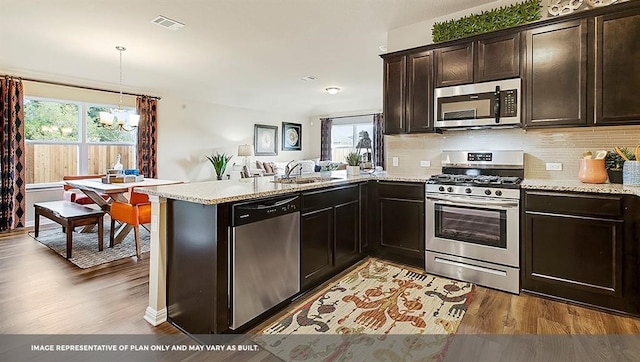 kitchen featuring appliances with stainless steel finishes, hanging light fixtures, kitchen peninsula, dark brown cabinets, and hardwood / wood-style floors