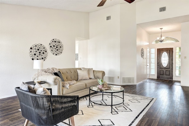 living room with a towering ceiling, a textured ceiling, ceiling fan with notable chandelier, and dark hardwood / wood-style floors