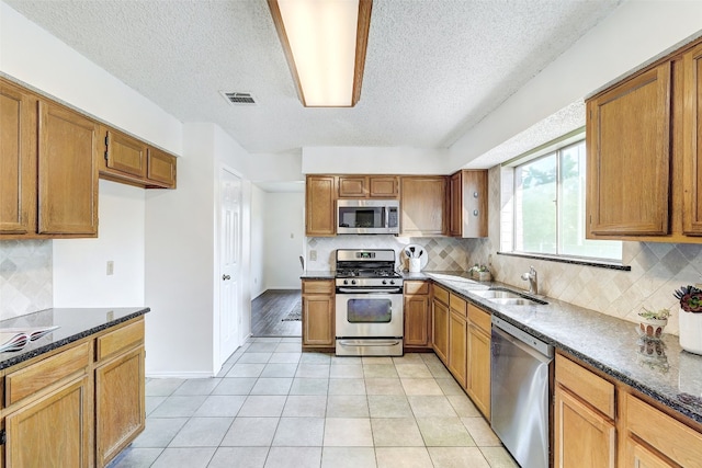 kitchen featuring appliances with stainless steel finishes, backsplash, dark stone countertops, and sink