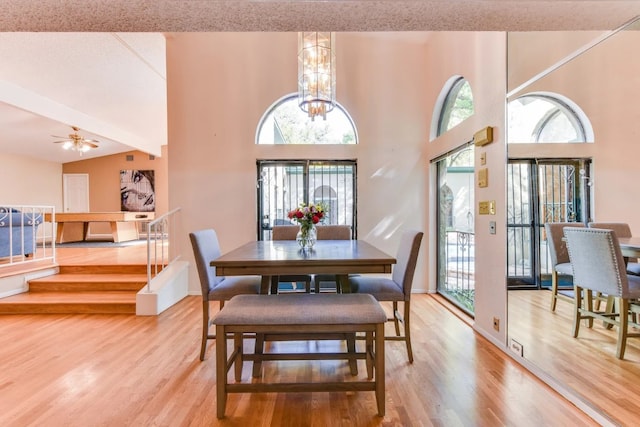 dining area featuring ceiling fan with notable chandelier, beam ceiling, light hardwood / wood-style flooring, and high vaulted ceiling