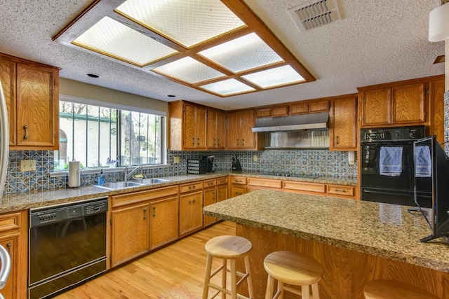 kitchen with tasteful backsplash, a breakfast bar area, black appliances, light hardwood / wood-style flooring, and sink