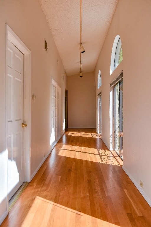 hall with a textured ceiling, a towering ceiling, and hardwood / wood-style floors