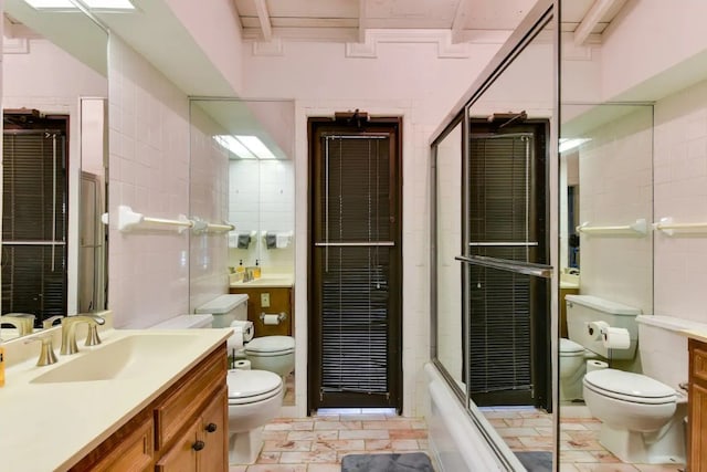 full bathroom with bath / shower combo with glass door, vanity, tile walls, and toilet