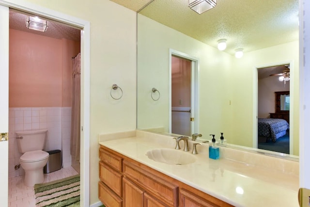 bathroom with tile walls, tile patterned flooring, a textured ceiling, vanity, and toilet