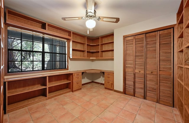 unfurnished office featuring ceiling fan, light tile patterned flooring, and built in desk