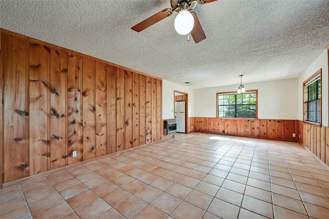 tiled spare room featuring wooden walls, a textured ceiling, and ceiling fan