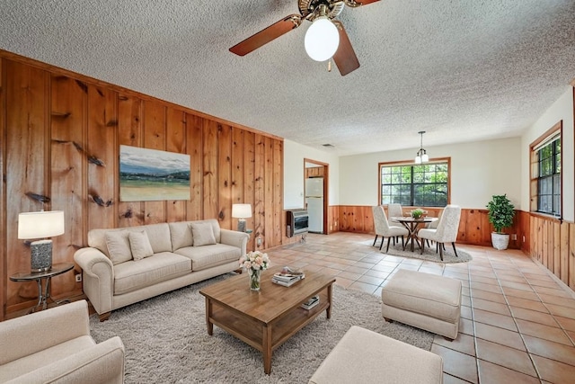 living room with a textured ceiling, wooden walls, and ceiling fan