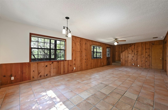 unfurnished room with light tile patterned flooring, wooden walls, ceiling fan, and plenty of natural light