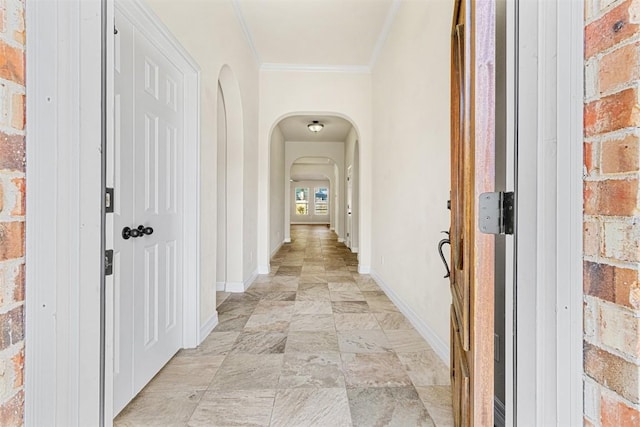 hall featuring baseboards, arched walkways, stone finish flooring, and ornamental molding