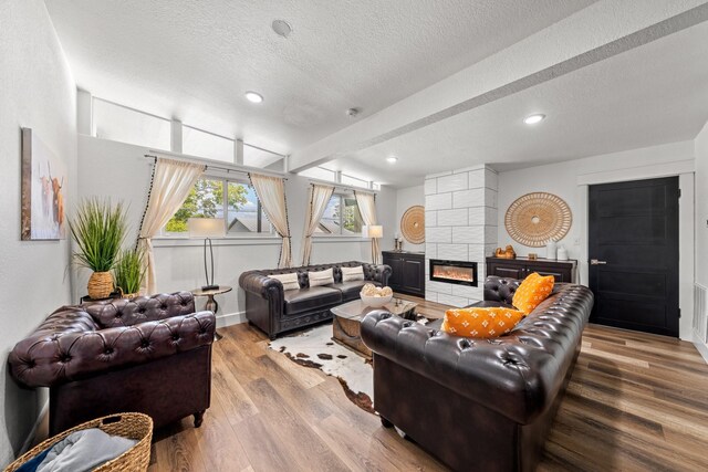 living room with beam ceiling, a tiled fireplace, a textured ceiling, and light hardwood / wood-style flooring