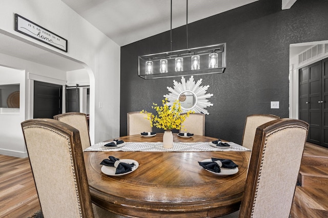 dining room featuring hardwood / wood-style floors, a barn door, and vaulted ceiling