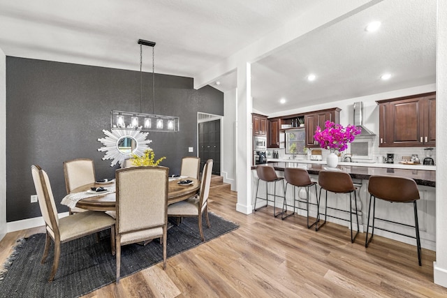 dining room featuring a textured ceiling, lofted ceiling, and light hardwood / wood-style floors