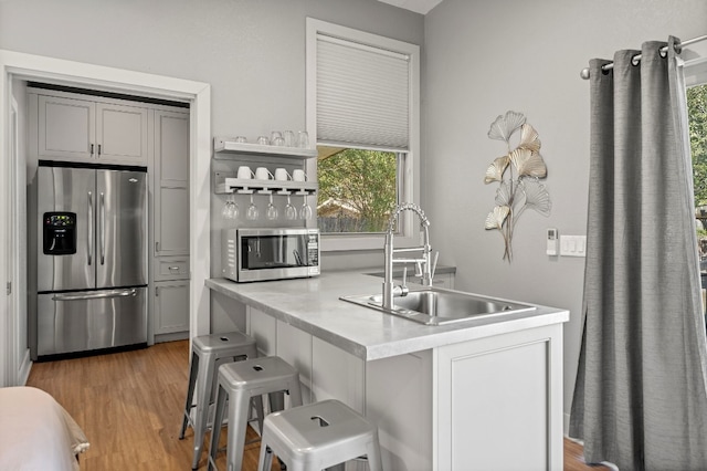 kitchen featuring a breakfast bar, appliances with stainless steel finishes, gray cabinetry, and sink