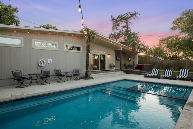 back house at dusk featuring a fenced in pool and a patio